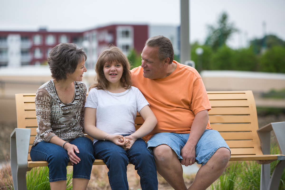 Family of three sit on a bench with daughter in the middle