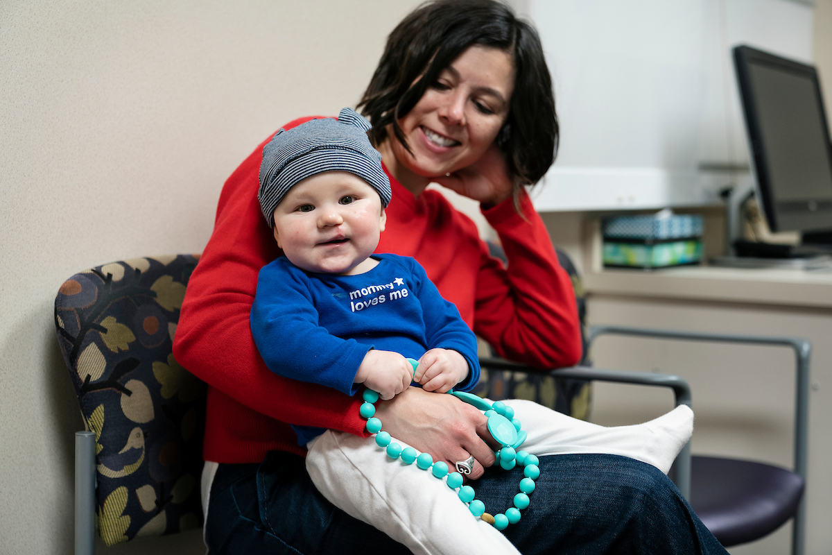 An infant patient at Gillette Children's during a clinic visit sit on his mothers lap.