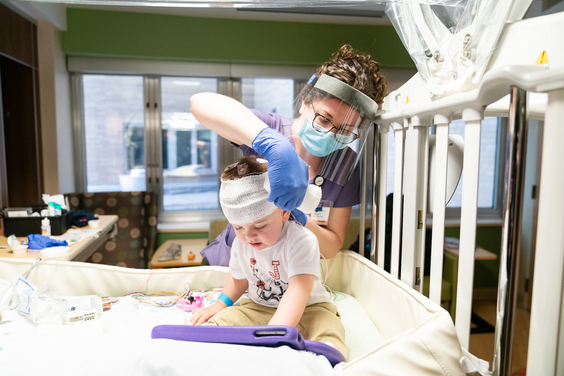 Jack S. a VEEG neurology patient at Gillette Children's gets a head wrap from a nurse after a procedure.