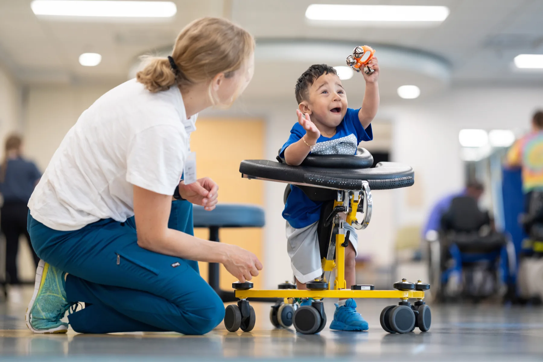 Small boy in a walker with therapist - Gillette Children's.