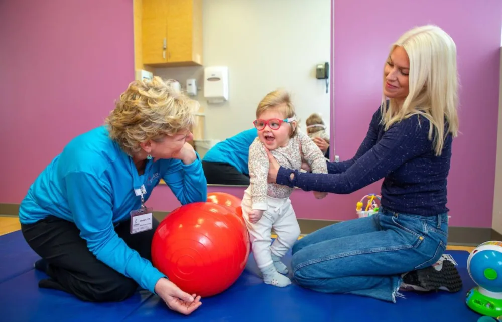 Elliana's mother, Rachel, holds Elliana in a standing position next to OT Wendy at Gillette Children's.