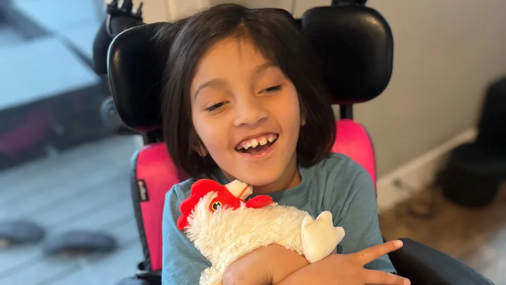 Gillette Children's patient Hazel Kim smiles while holding a stuffed animal in the shape of a chicken.
