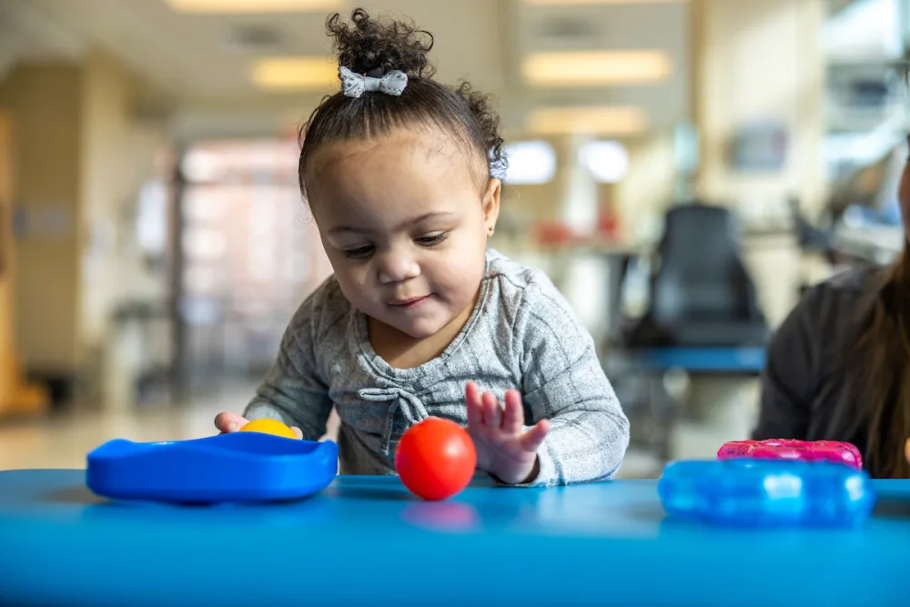 A young girl reaches for a toy as she works on her motor skills in the Gillette Children's rehab gym