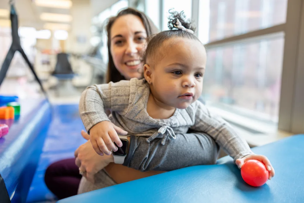 A Gillette Children's physical therapist holds a young girl as she works on her motor skills.