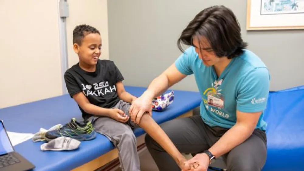 Zakariya sits on an exam table while a Gillette Children's physical therapist examines his leg.