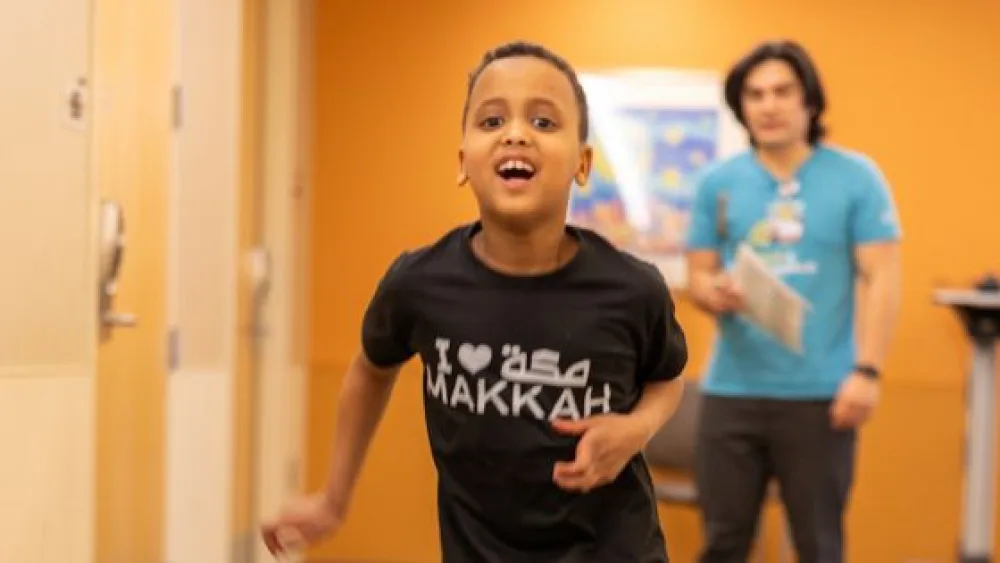 Zakariya smiles as a Gillette physical therapist watches him walk down a hallway.
