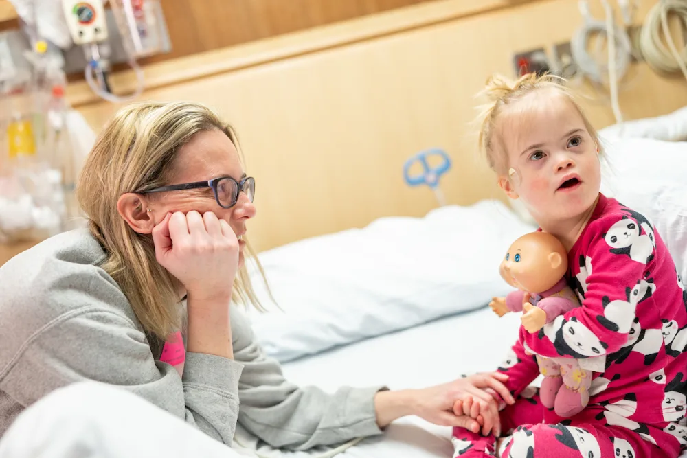 A young girl holds a doll and her mother looks on as they wait in the Gillette Children's sleep clinic room.