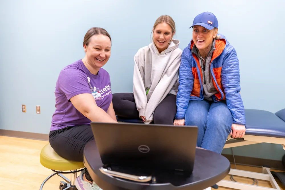 Maggie, her mother and physical therapist look at a lap top image of her spine.