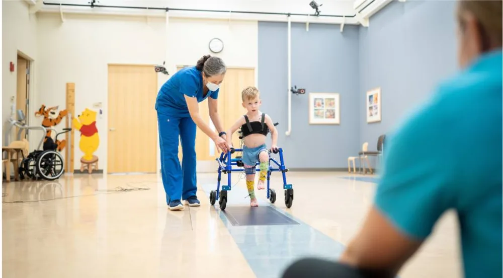 Child in walker with provider  - Gillette Children's.