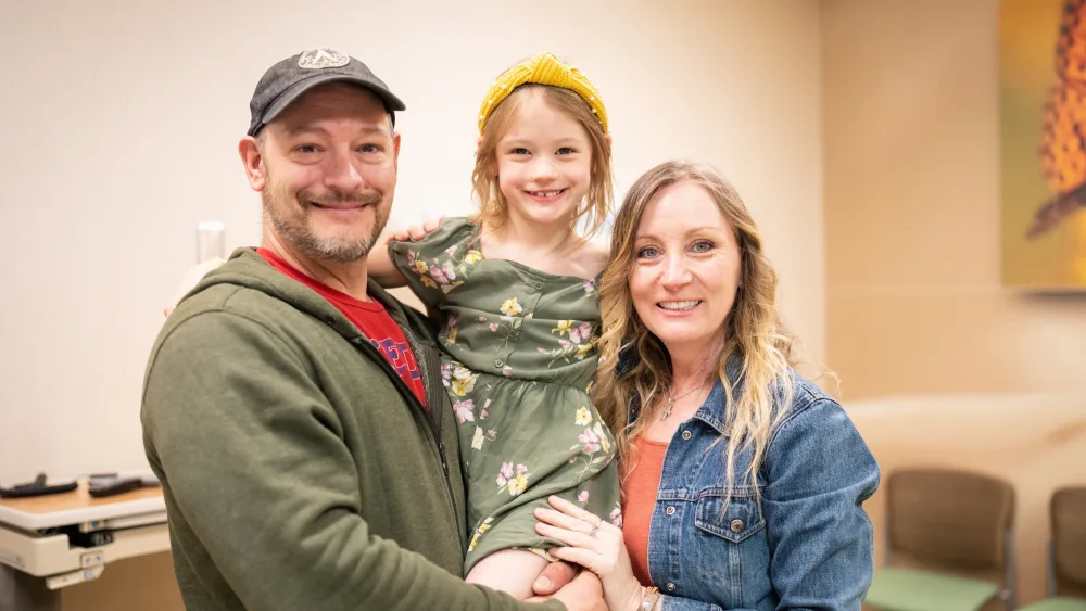 A man, a five year old girl, and a woman pose for a family portrait in an exam room at Gillette Children's.
