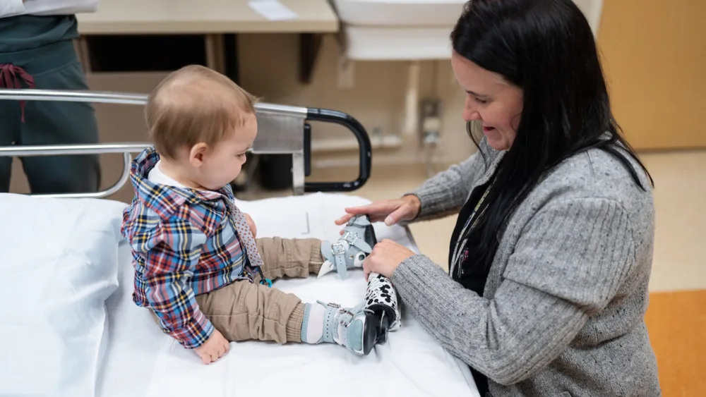 Wyatt Krentz tries on the boots and bar apparatus meant to treat clubfoot.