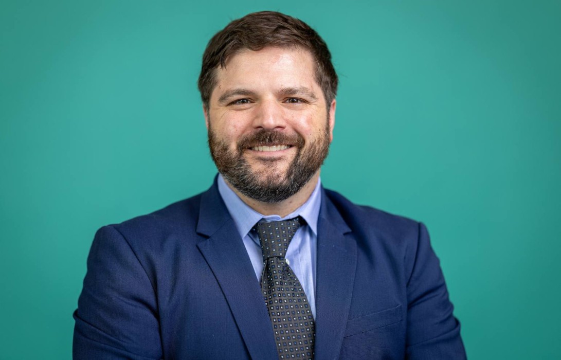 Gillette Children's neurologist Bryan Mendes smiles for a portrait against a teal background.