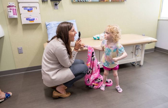 A physician crouches down to be eye level with a young female patient inside an exam room at Gillette Children's.