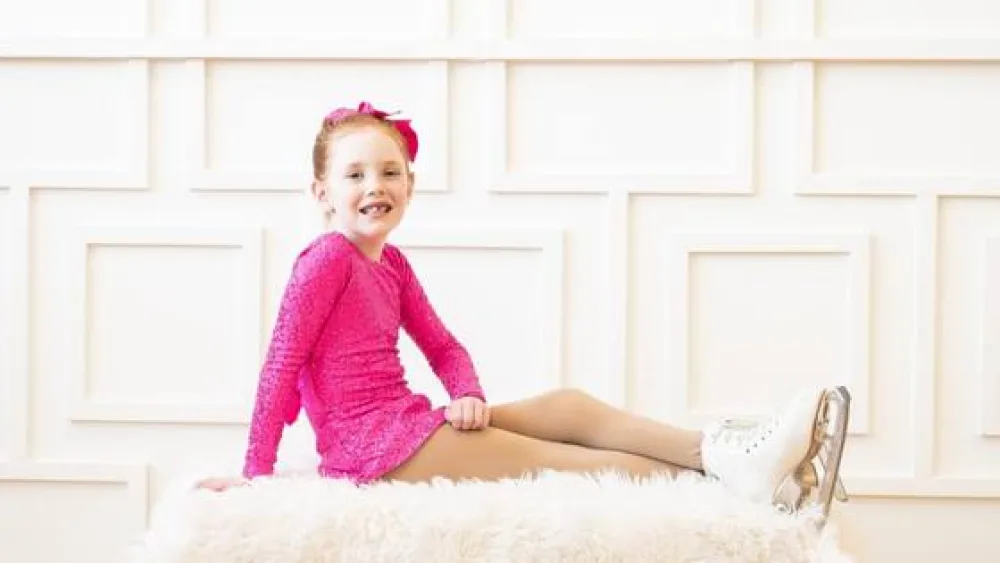 Girl in ice skates posing for portrait on a fluffy rug  - Gillette Children's.