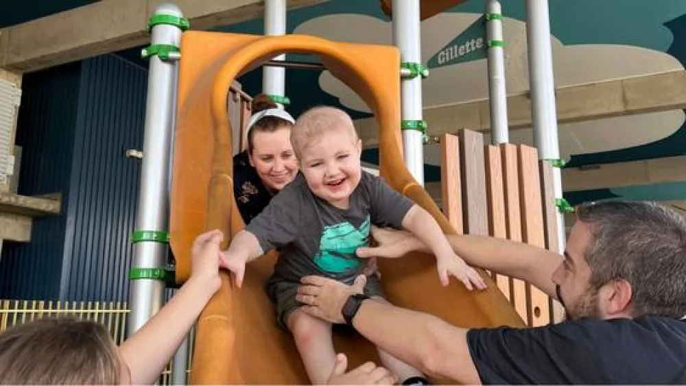 Two children being helped down a slide  - Gillette Children's.