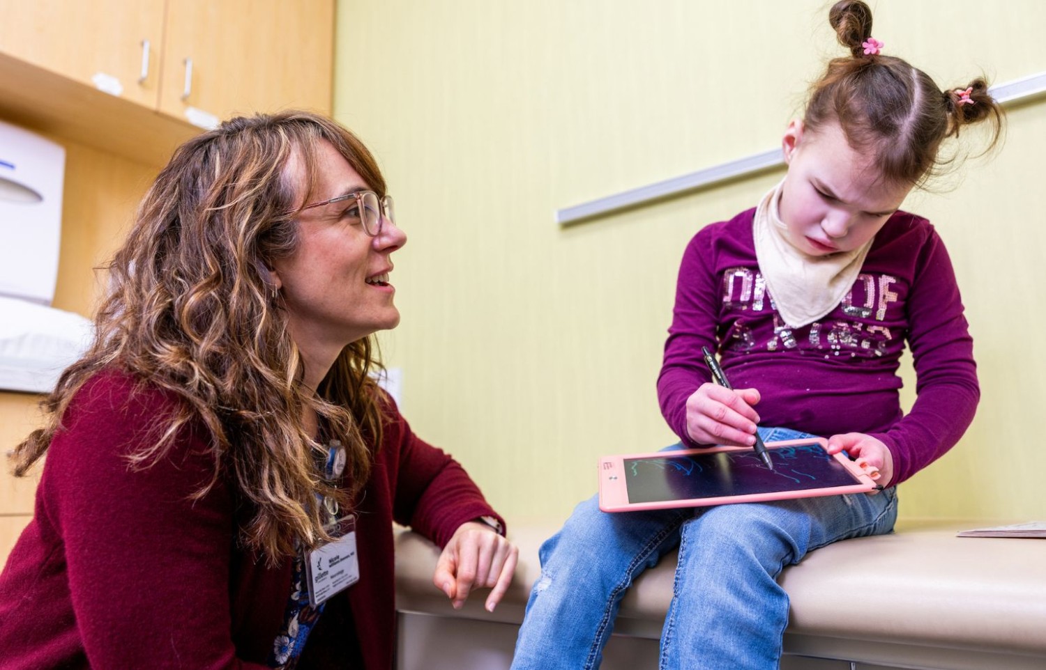 A provider kneels next to a pediatric patient in an exam room at Gillette Children's.