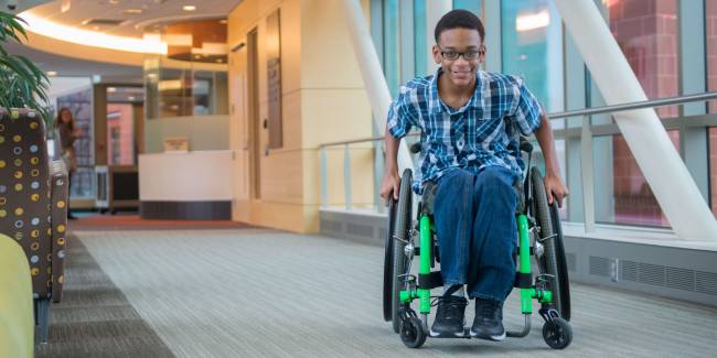 Gillette patient Elijah using wheelchair near rehab therapies in skyway.
