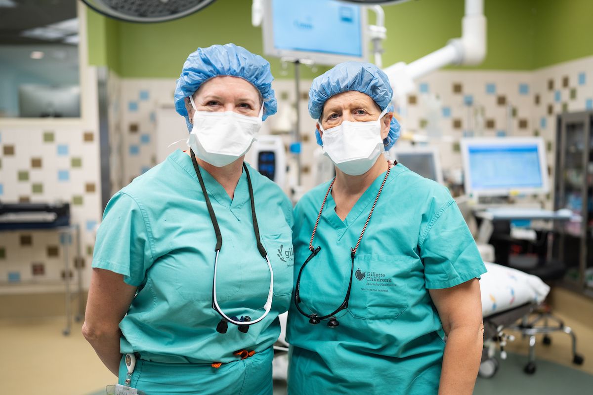 Orthopedic surgeons, Deborah Bohn, MD and Ann Van Heest, MD standing together in scrubs in the Gillette operating room.