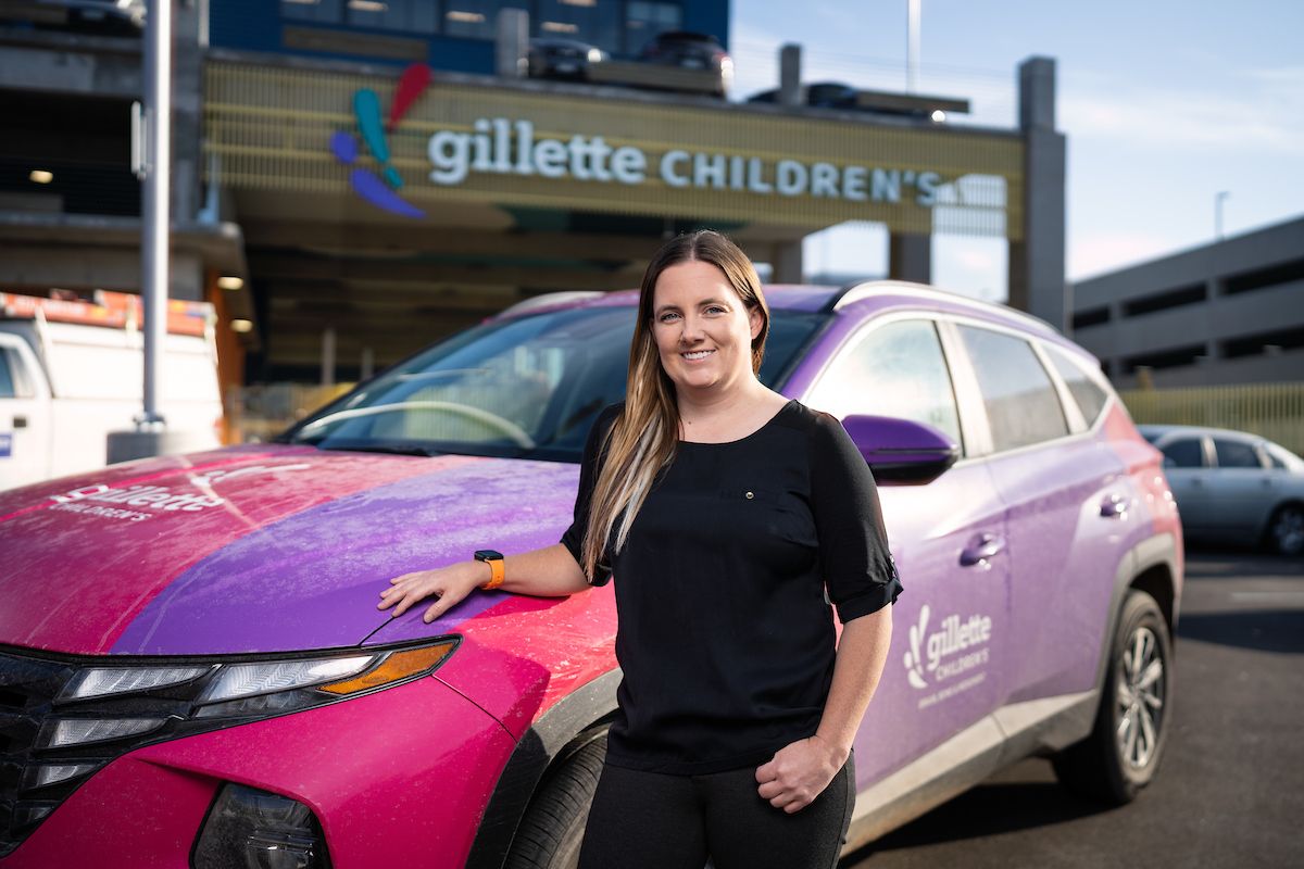 Andrea Paulson, MD, drives hundreds of miles each month to see Gillette Children's patients throughout Greater Minnesota. She is standing near a Gillette-branded car.