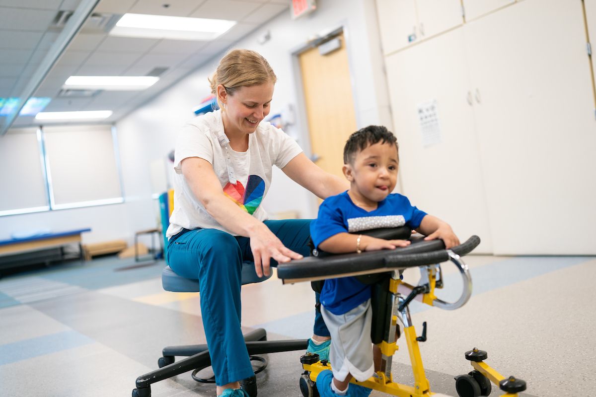 Ernesto and his Gillette physical therapist (PT), Katherine Kaiser, practice walking in a gait trainer.