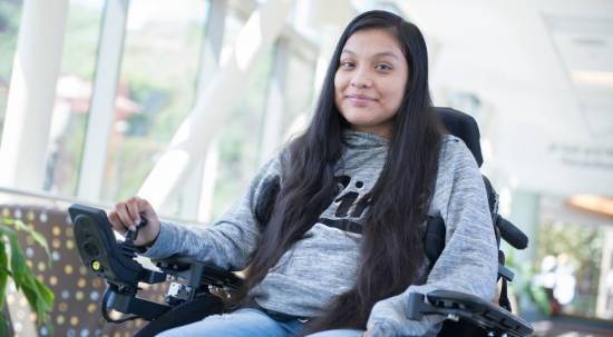 Guadalupe Galeno Hernandez sits in her motorized wheelchair and smiles for the camera in the skyway at Gillette Children's.