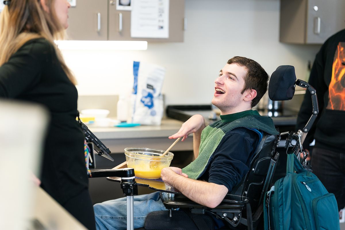 teen boy in a power chair stirring in a bowl while cooking in the classroom