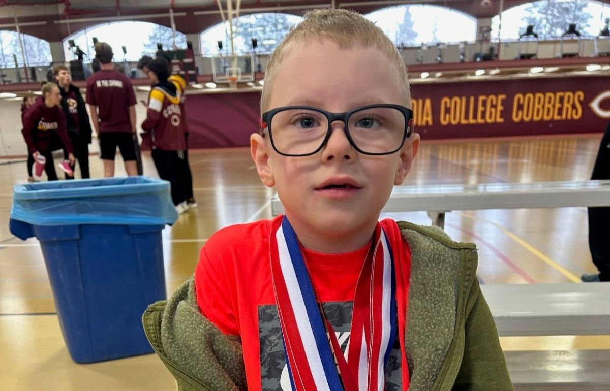 Owen is standing in a gym and is proud of the medals he won.